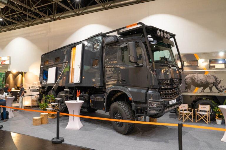 Dunkles Allrad-Expeditionsmobil auf Mercedes-Arocs-Basis, dahinter ein Aufbau mit Nashorn-Motiv