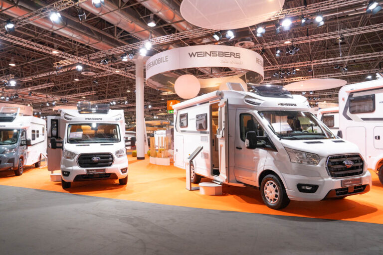 Messestand von Weinsberg mit weißen Teilintegrierten auf Ford-Basis und orangefarbenem Boden