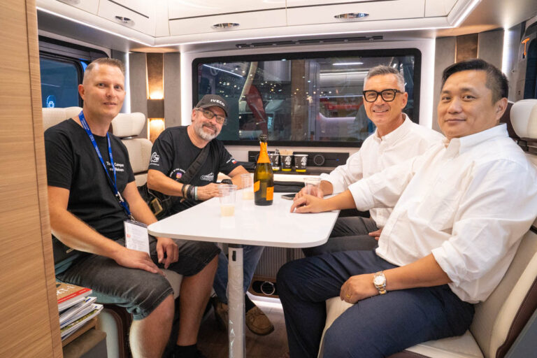 Vier Personen sitzen an der Sitzgruppe eines Reisemobils und stoßen miteinander an