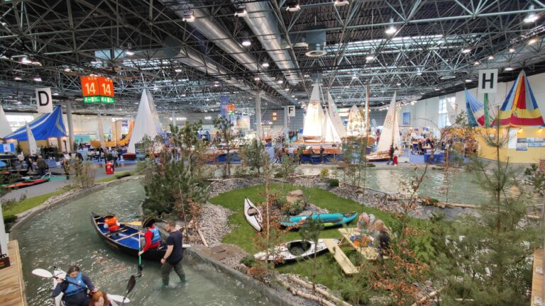 Wasserbecken in der Messehalle mit Kanus und Segelbooten sowie einer bepflanzten Insel