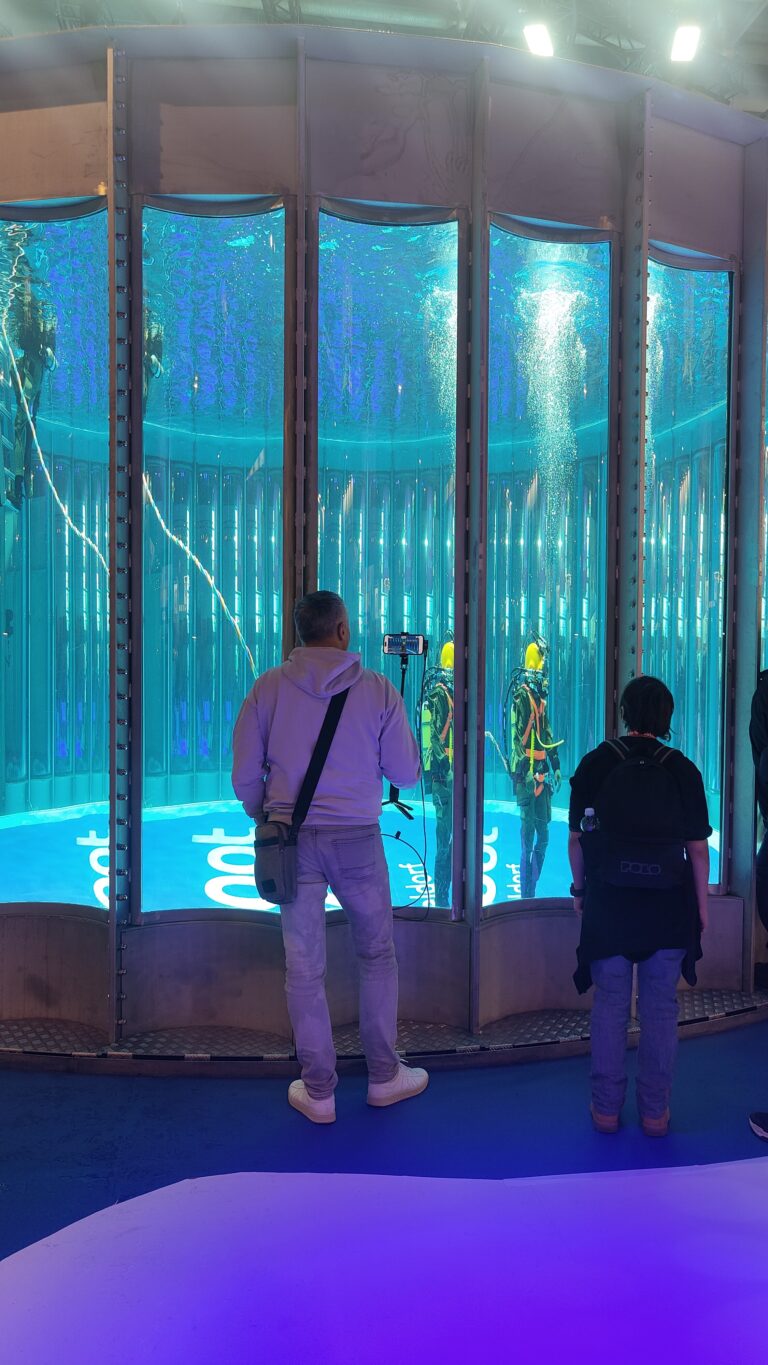 Zwei Besucher beobachten durch die Panoramascheiben des Tauchturms zwei Taucher unter Wasser