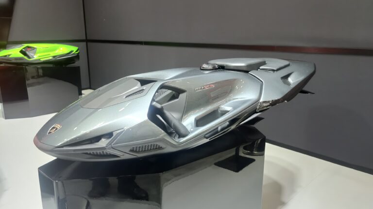 Graues Wassermotorrad im Lamborghini-Design auf einem Podest, dahinter ein grünes Modell